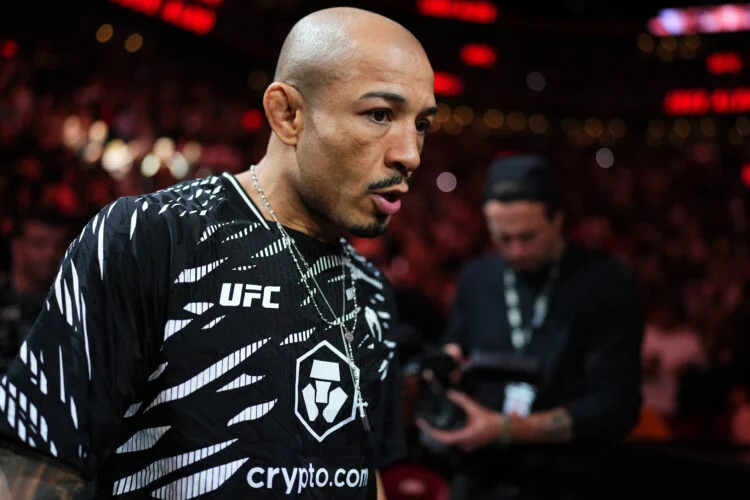 MMA fighter in a black UFC jersey on a lit arena floor, focused and looking to the side.