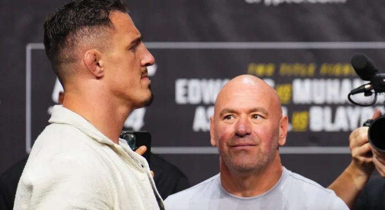 Two men at a weigh‑in event: a left-facing man in a light jacket beside a bald man in a gray shirt, with a banner behind them.
