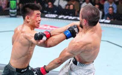 Two UFC fighters clash in the octagon; one has a bloody cut on his face while landing a punch on his opponent inside the cage.