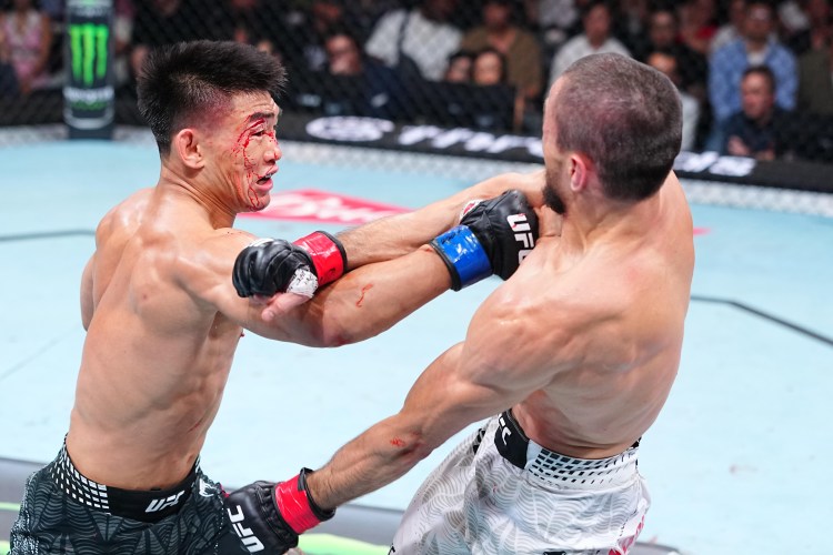 Two UFC fighters clash in the octagon; one has a bloody cut on his face while landing a punch on his opponent inside the cage.