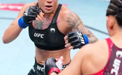 Female UFC fighter in black gear throws a punch toward her opponent in a match.