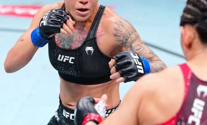 Female UFC fighter in black gear throws a punch toward her opponent in a match.