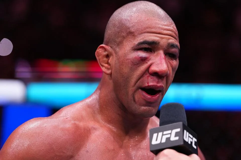 Bald UFC fighter with a bloody nose speaks into a microphone after a fight during a post-fight interview.