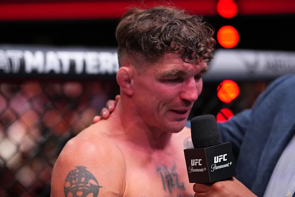UFC fighter being interviewed in the cage, holding a microphone with UFC Paramount+ logo in front of him after a fight.