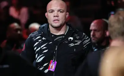 Bald man wearing a black patterned hoodie with a lanyard and event ID badge, in a crowded arena.