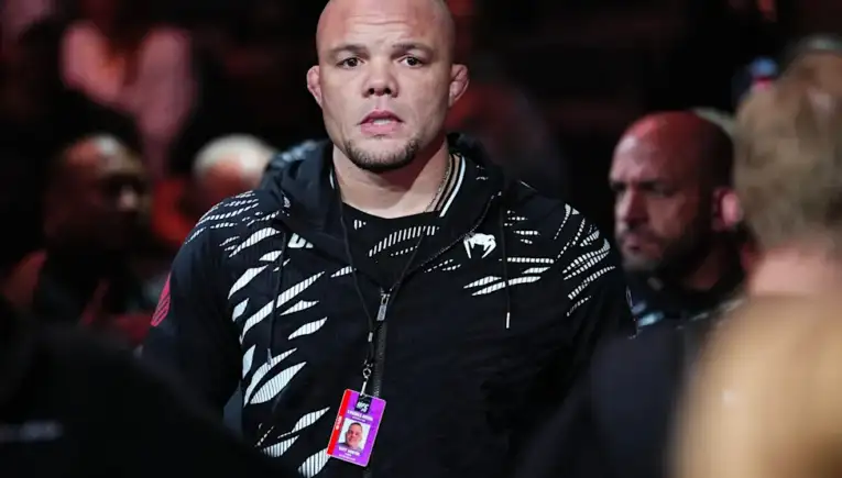 Bald man wearing a black patterned hoodie with a lanyard and event ID badge, in a crowded arena.