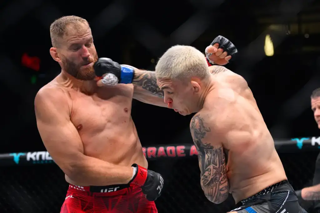 Two shirtless mixed martial artists clash in a cage, one lands a punch to the other's bleeding nose.
