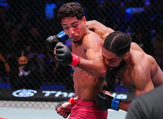 Two male mixed martial artists battle inside a fenced cage; one lands a punch to the other’s face while the other clinches him.