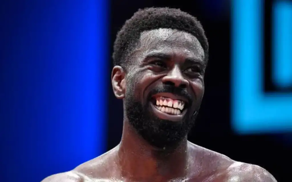 Chidi Njokuani_20260817_020158_0000 - AfroCombat Close-up of a smiling man with a beard, sweat on his face, on a stage with blue lighting in the background