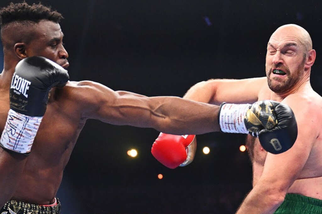 A muscular boxer on the left throws a straight punch toward the bald opponent on the right during a match.
