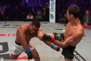 Screenshot-2026-07-31-at-90526-PM - AfroCombat Two male mixed martial artists in a cage-like ring, one delivering a high kick to the other’s head while the opponent braces for impact, with spectators in the background.