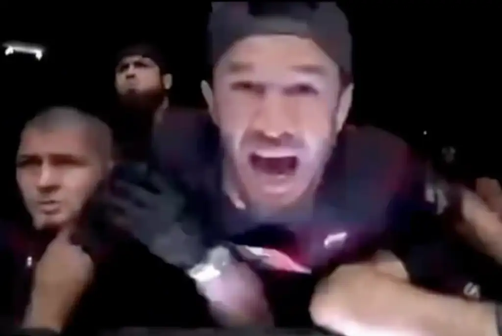 Man wearing a cap shouting with mouth open in a crowded nighttime scene.
