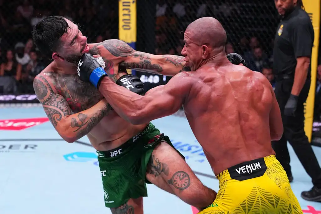 Two UFC fighters clash in the octagon; one lands a punch to the other’s face while the green shorts fighter guards with his arms.