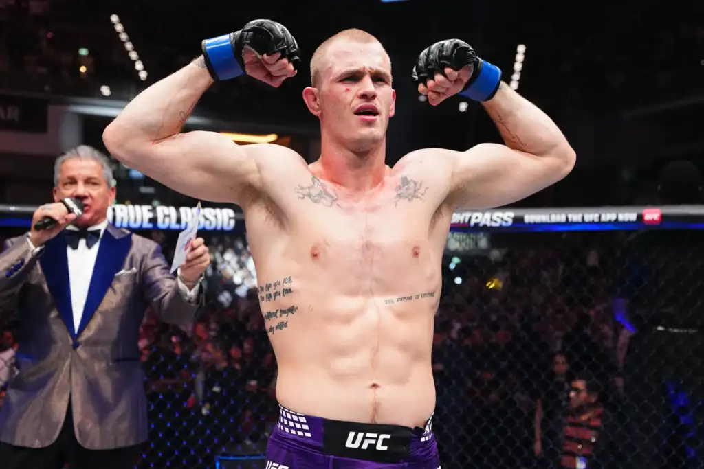 UFC fighter raising fists in victory inside the octagon, referee in background and cheering crowd behind him