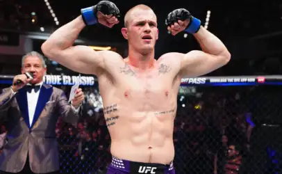 UFC fighter raising fists in victory inside the octagon, referee in background and cheering crowd behind him