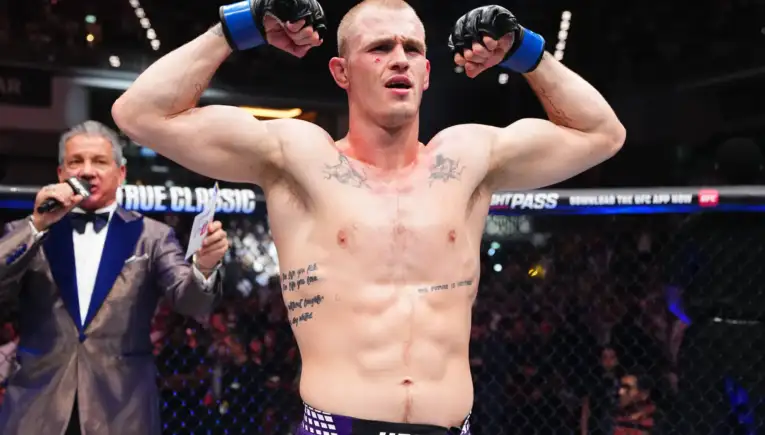 UFC fighter raising fists in victory inside the octagon, referee in background and cheering crowd behind him