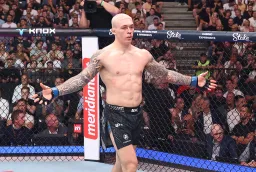 gettyimages-2288626850 - AfroCombat MMA fighter stands shirtless with arms outstretched inside the fenced octagon as a crowd watches.