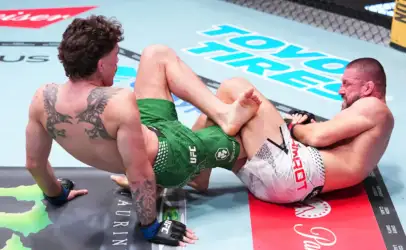 Two shirtless mixed martial artists grappling on a UFC-style mat, one with a large back tattoo and green shorts, the other in white shorts.