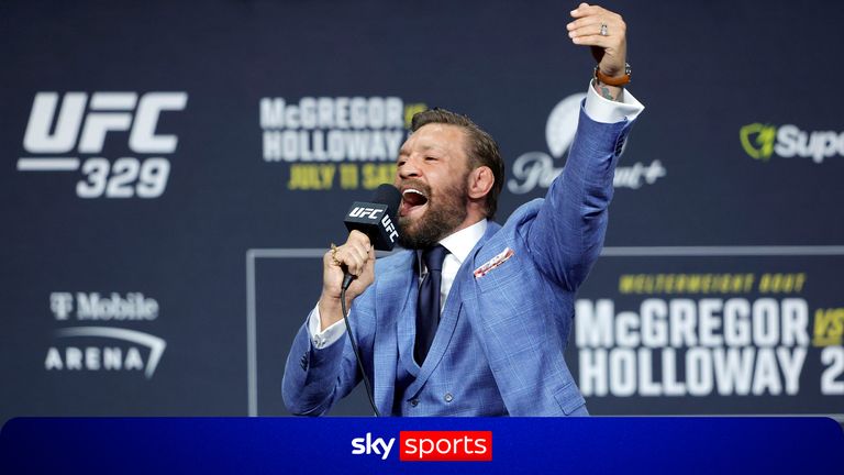 Male presenter in a blue suit on stage at a UFC event, holding a microphone and raising his fist in celebration.