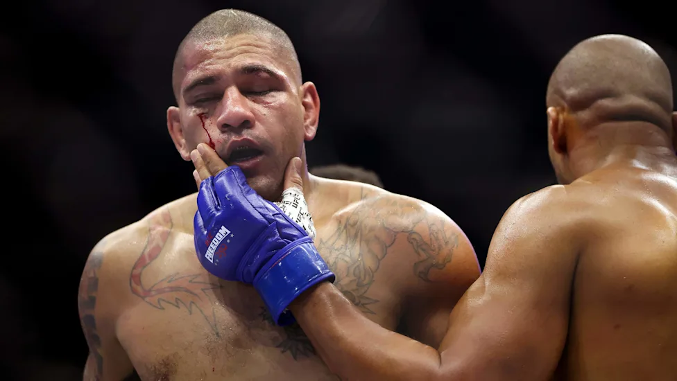 Boxer with blue gloves shows a bloodied face as an opponent touches his cheek during a fight.
