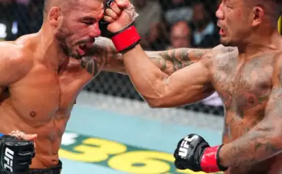 Two shirtless UFC fighters clash in the octagon; one punches the other, blood smeared on the face and a determined crowd in the background.