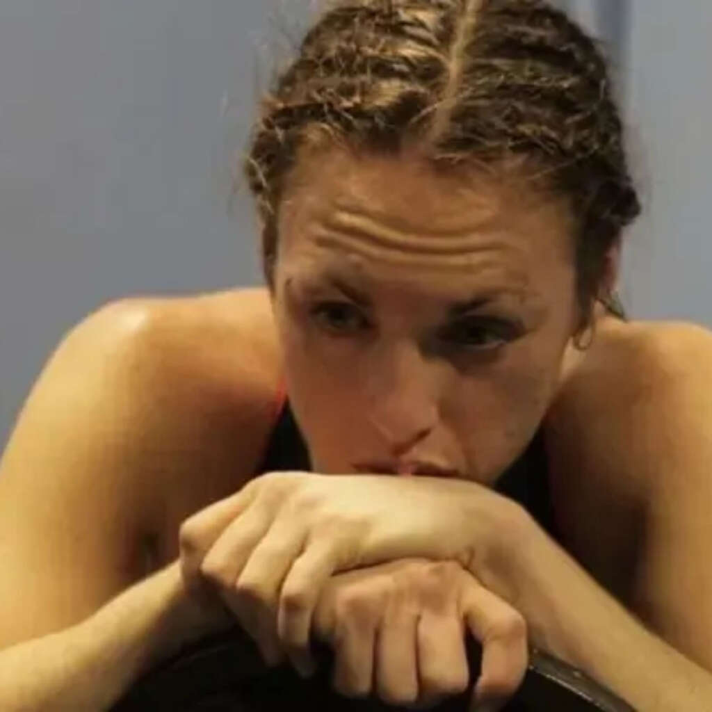Woman with hair tied back rests her chin on her folded arms, looking downward.