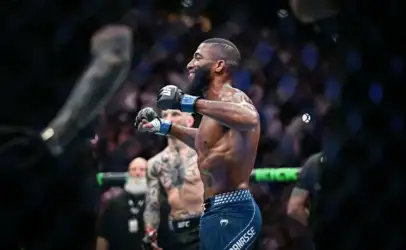 UFC fighter in blue shorts celebrating with fists up inside the octagon, crowd in background.