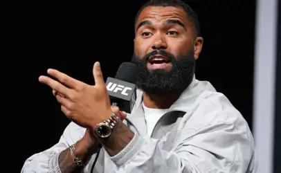 Bearded man speaks into a UFC-branded microphone, gesturing with his hands during a press event.