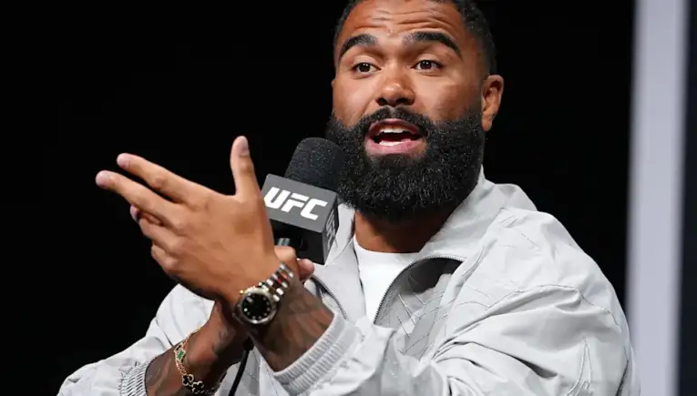 Bearded man speaks into a UFC-branded microphone, gesturing with his hands during a press event.