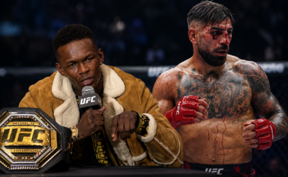 UFC post-fight interview: a man in a brown shearling coat speaks into a mic beside the UFC belt on the table, while a bloodied, tattooed fighter stands with red gloves nearby.