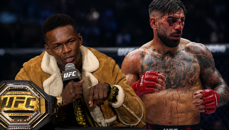 UFC post-fight interview: a man in a brown shearling coat speaks into a mic beside the UFC belt on the table, while a bloodied, tattooed fighter stands with red gloves nearby.