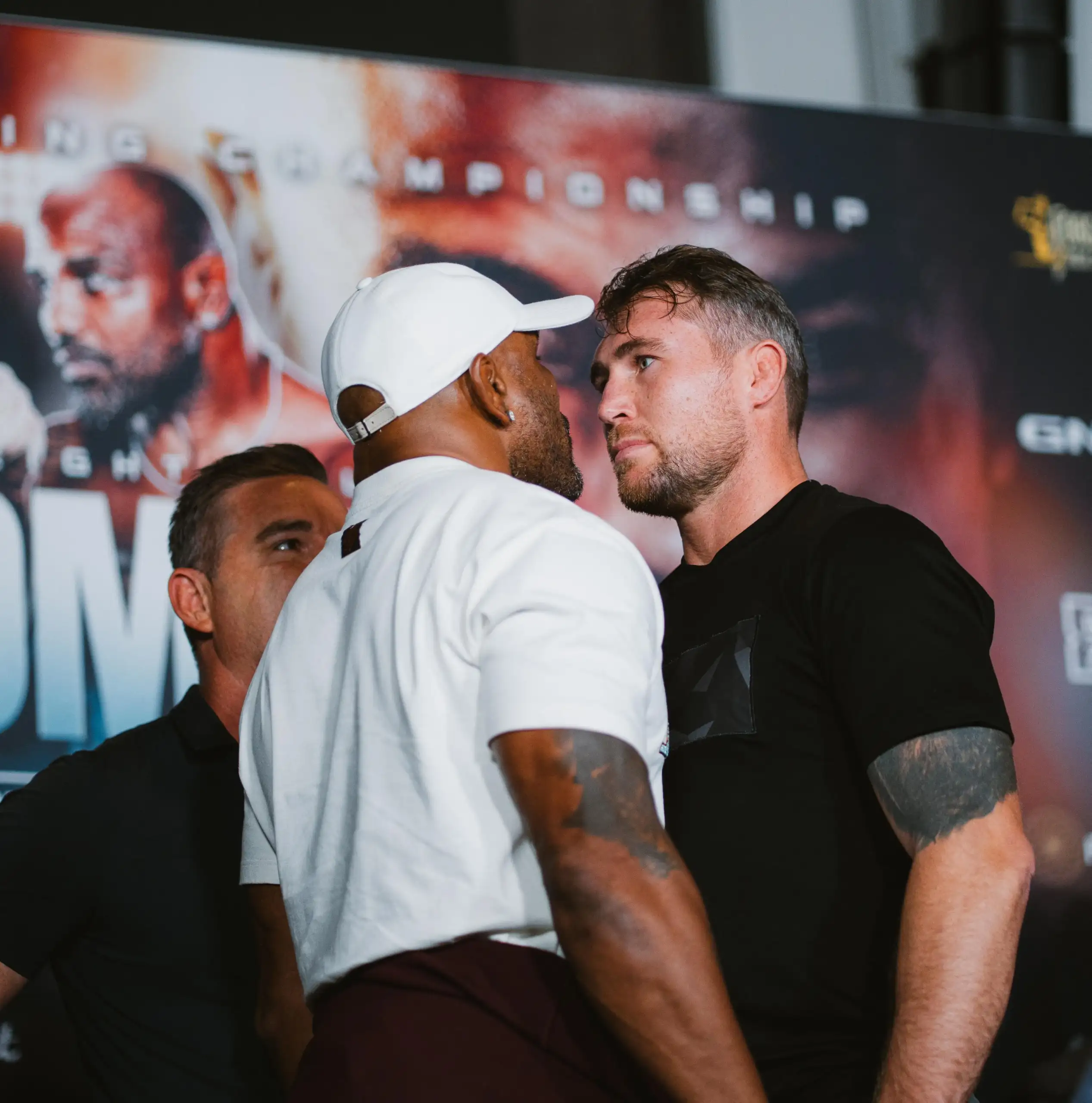 Two men in casual clothes lean in toward each other in a close pose at a media event, with a banner behind them.