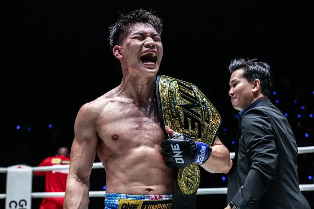 Rambolek-Chor-Ajalaboon-Nabil-Anane-Superfan-Fights-5-scaled - AfroCombat Male mixed martial artist shouts in celebration, holding a gold championship belt over his shoulder inside a boxing ring.
