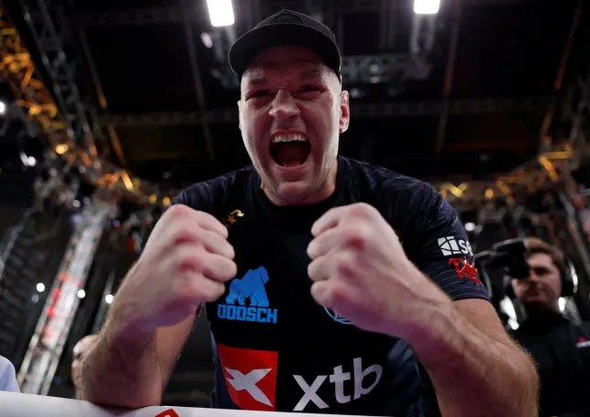 Athlete in a cap shouting with fists clenched in front of him inside a stadium arena of bright lights.
