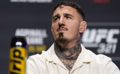 Male mixed martial artist with a tattooed neck wearing a cream button-up shirt at a UFC press event. (informative)