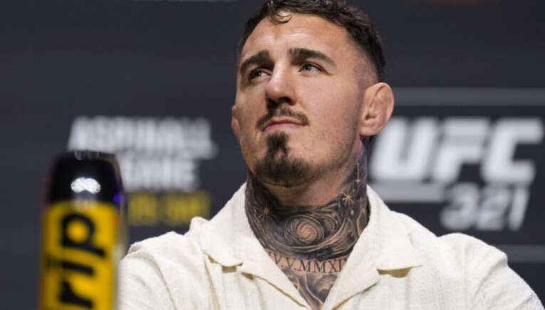 Male mixed martial artist with a tattooed neck wearing a cream button-up shirt at a UFC press event. (informative)
