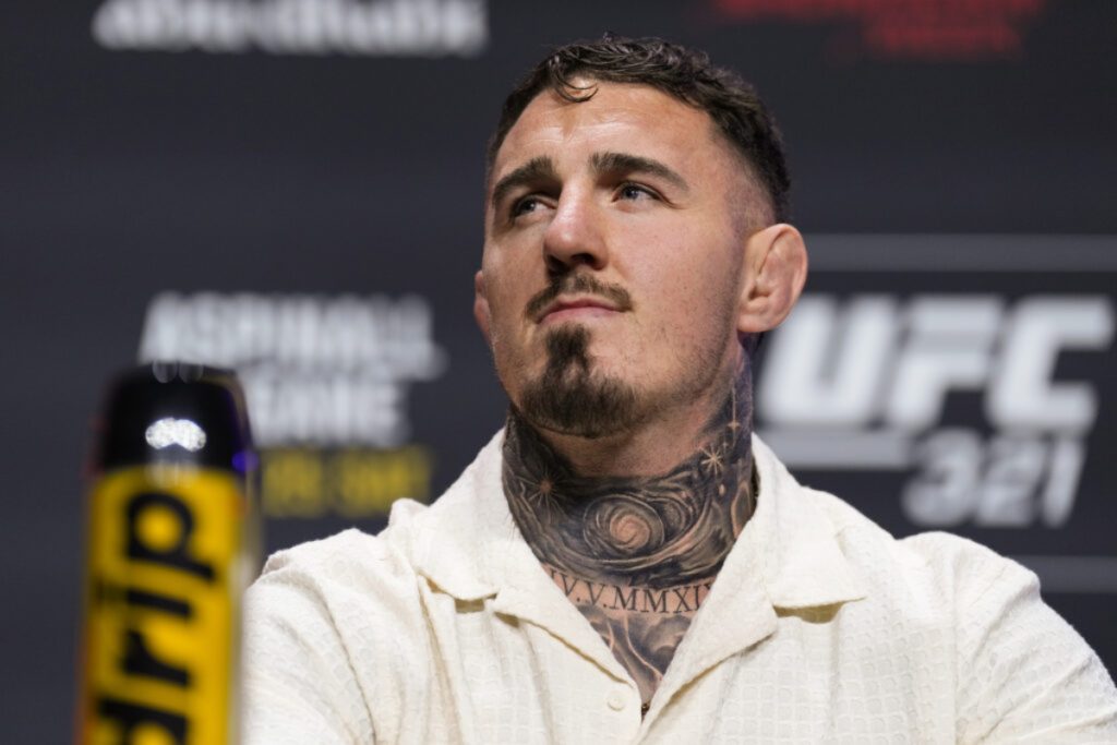 Male mixed martial artist with a tattooed neck wearing a cream button-up shirt at a UFC press event. (informative)