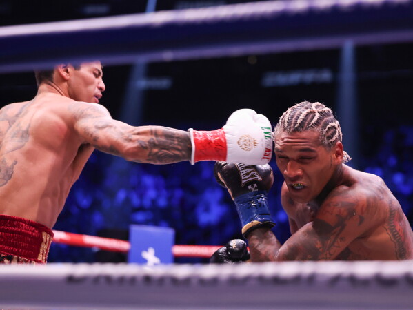 download 1 - AfroCombat Boxer in red shorts and gloves throws a punch at a rival with cornrowed hair and blue gloves inside a boxing ring.