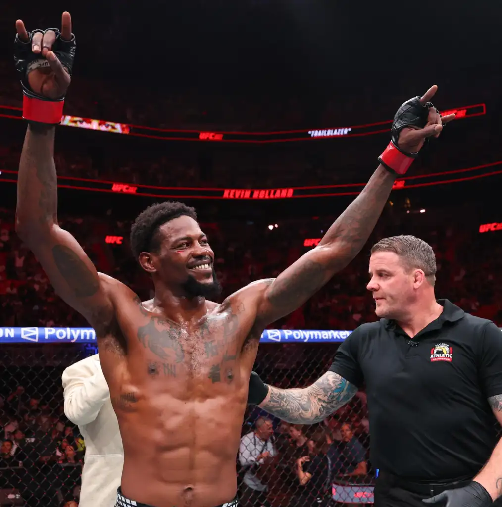 Two victorious mixed martial artists raise their gloved arms in celebration inside a UFC ring, with a cheering crowd in the background.