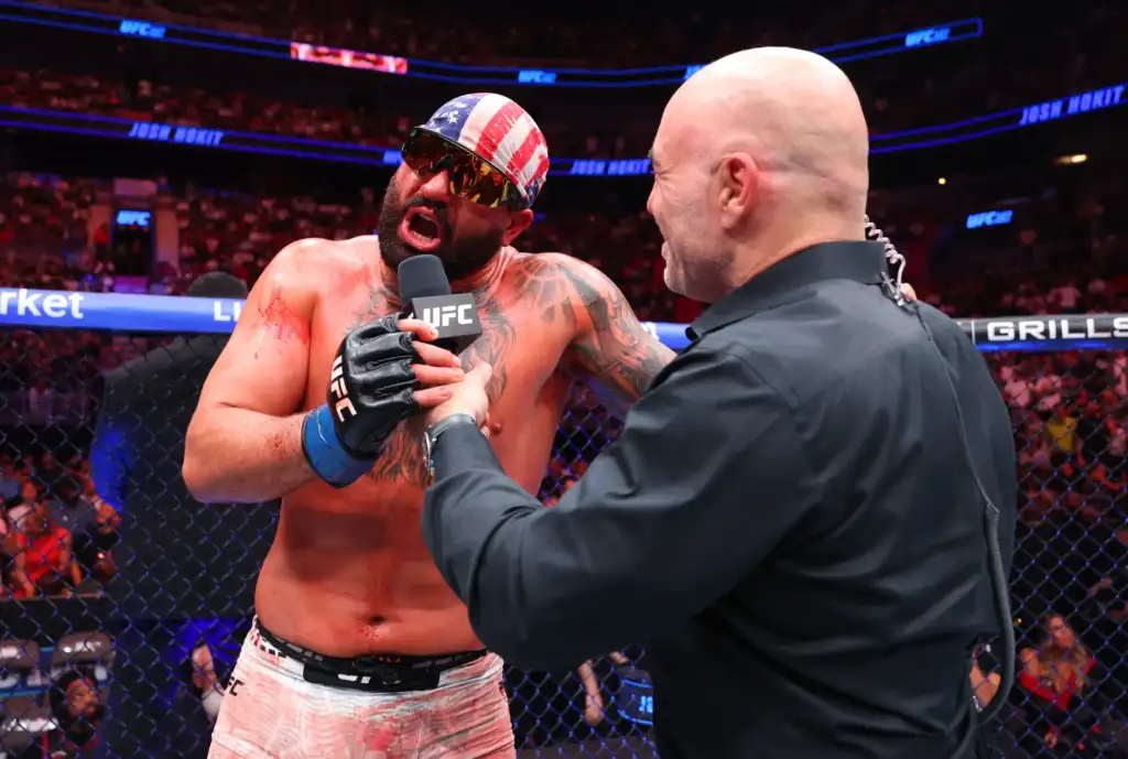 UFC fighter with an American flag bandana being interviewed inside the cage, speaking into a microphone.