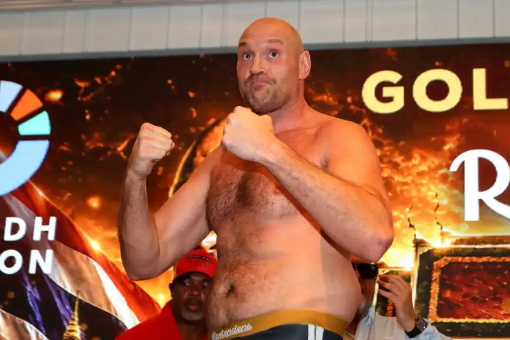 Bodybuilder/boxer on stage in fighting stance, shirtless, with fiery backdrop and crowd watching.