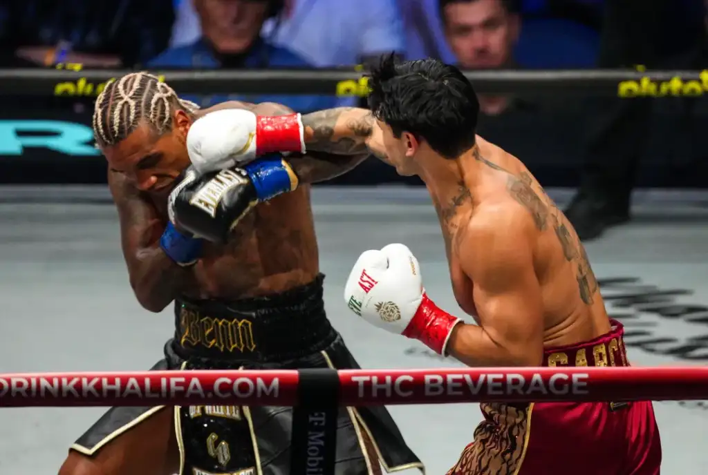 Two shirtless boxers in a ring exchange punches while a crowd watches; the fighter on the left covers up as the right-handed punch lands near his head.