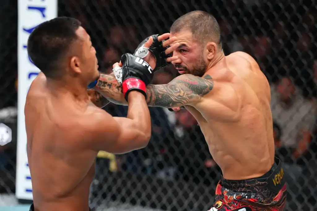 gettyimages-2296159880 - AfroCombat Two shirtless MMA fighters in a UFC-style cage exchange strikes during a match, one delivering a punch toward the other's face.
