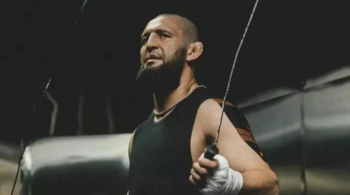 Athlete with a beard in a black sleeveless shirt and hand wraps grips jump rope in a gym setting.