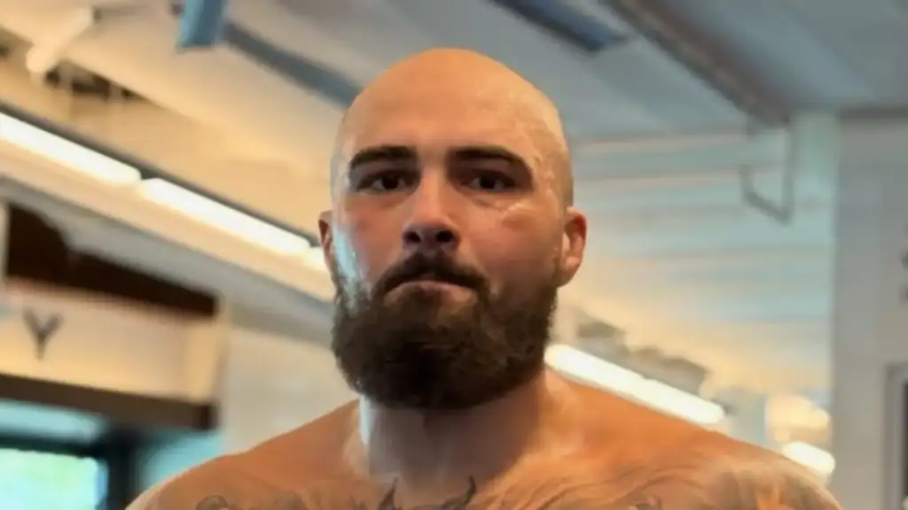oe8oq1so_ufc-331-takes-wild-turn-as-sean-sharaf-floors-gable-steveson-in-12-seconds_625x300_20_September_26 - AfroCombat Bald man with a full beard standing shirtless in a gym, looking at the camera with a serious expression, tattoos visible on his chest and shoulders with gym equipment in the background