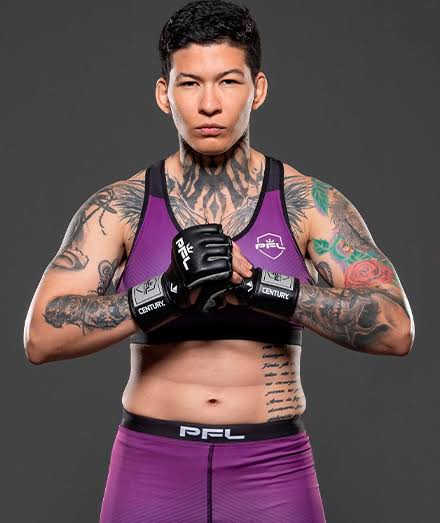 Female mixed martial artist in a purple sports bra and shorts, fists raised in front, tattooed arms and chest, neutral gray background.