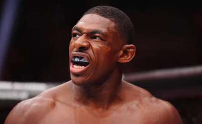 UFC fighter roars with mouthguard showing, bare shoulders in a fighting ring.