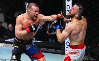 Two UFC fighters exchange punches in the cage: one lands a left hook while the other blocks his face with a guard, inside the octagon.