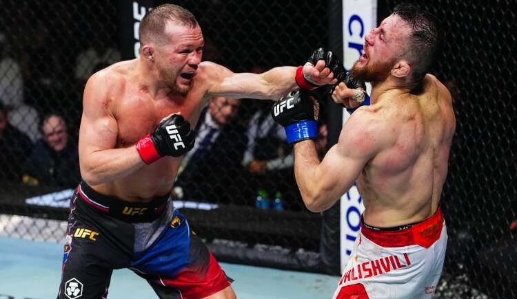 Two UFC fighters exchange punches in the cage: one lands a left hook while the other blocks his face with a guard, inside the octagon.