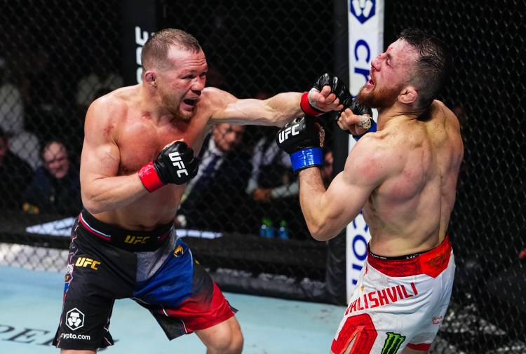 Two UFC fighters exchange punches in the cage: one lands a left hook while the other blocks his face with a guard, inside the octagon.